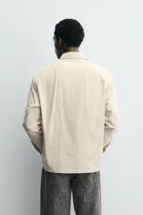 Camisa polo de corte relajado confeccionada en algodón, con estampado de rayas verticales finas. Presenta cuello solapa, cierre frontal parcial con botones, bolsillo plastrón en el pecho y mangas largas con puños abotonados.