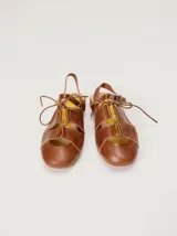 Sandalias planas tipo slingback de cuero marrón, con diseño delantero calado, cierre de cordones y tira trasera ajustable con hebilla.