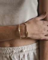 Brazalete rígido abierto de metal color plateado con textura irregular.