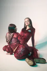 Conjunto de dos piezas compuesto por una campera con capucha y cierre frontal, y un pantalón de corte acampanado. Ambas prendas están confeccionadas en tela de terciopelo con estampado de animal print en tonos rojizos. La campera presenta un logo circular en el pecho y una estrella grande con apliques de strass en la espalda, mientras que el pantalón incluye una estrella de strass en la parte trasera.