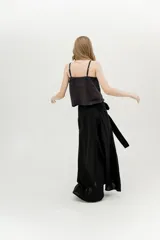 Falda larga negra, estilo envolvente o pareo, con abertura frontal alta y lazo ajustable en la cintura.