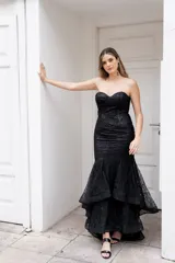 Vestido largo negro strapless tipo corset con tul y lentejuelas, de corte sirena y falda con volados.