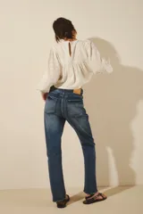 Jean de corte recto y tiro alto, confeccionado en denim azul con un lavado localizado que presenta efecto de bigotes y torceduras. Cuenta con cierre y botón frontal.