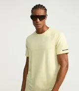 Remera deportiva de hombre con tecnología dry fit, cuello redondo y manga corta. Presenta un diseño liso en color beige con una pequeña etiqueta decorativa en el dobladillo.