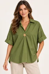 Camisa de algodón color verde militar, con cuello camisero, escote en V profundo y detalle de botón dorado en forma de flor. Mangas cortas con vuelta y diseño holgado.