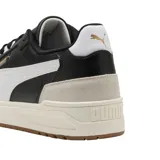 Championes Puma modelo Shuffle Downtown OG, de diseño urbano con base blanca, detalles en negro y suela de goma color caramelo. Presentan refuerzos en gamuza gris en la puntera y el talón, con el logo de la marca en dorado.