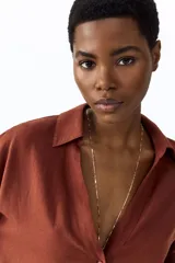 Camisa de mezcla de lino y viscosa color terracota, con cuello abierto, escote en V con botonadura frontal, hombros caídos y mangas tres cuartos holgadas.