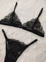 Conjunto de lencería de encaje negro, compuesto por un soutiene tipo triángulo con tirantes regulables y una bombacha colaless con tiras laterales ajustables mediante argollas metálicas.
