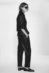 Chaqueta efecto piel color marrón, con cuello solapa, mangas por debajo del codo, cintura elástica, falsos bolsillos delanteros y cierre frontal con cremallera.