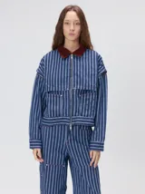 Campera de denim a rayas verticales con cuello de pana en color bordó. Presenta cierre frontal, mangas desmontables con cierre en los hombros, canesú en el pecho y bolsillos de parche cuadrados.