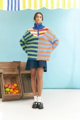 Sweater de tejido de punto grueso, cuello alto con cierre parcial y manga larga. Presenta un diseño de bloques de color y rayas horizontales en tonos vibrantes como azul, verde lima, naranja y celeste.