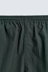 Pantalón jogger de corte relajado confeccionado en tejido técnico de color verde oscuro. Presenta cintura elástica con cordón interior, bolsillos laterales con cierre y bajo ajustable con elástico. Incluye detalles de líneas en contraste a lo largo de las piernas.