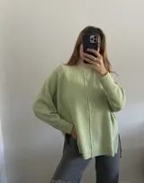 Sweater oversize de tejido liviano, color beige, con cuello redondo, mangas largas con puños acanalados y tajos laterales. Presenta una costura vertical decorativa en el frente y un diseño más largo en la parte posterior.