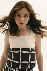 Top de tirantes anchos con diseño bicolor, presentando una parte superior en color crudo y una parte inferior estampada con un patrón geométrico de cuadrícula en negro y blanco.