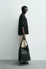 Camisa de corte relajado en color negro, confeccionada en tejido de algodón. Presenta cuello tipo bowling, manga corta y cierre frontal con botones. Cuenta con bordados lineales de hojas en la parte delantera.