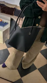 Cartera de cuero mediana con manijas largas, diseño con borde superior en corte en V y terminación artesanal con costuras contrastantes.