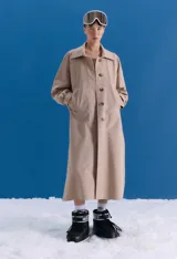 Trench midi color camel, confeccionado en mezcla de algodón y nylon. Presenta cuello clásico, cierre frontal con botones, tajos laterales y bolsillos internos. Es una prenda repelente al agua con diseño versátil y funcional.