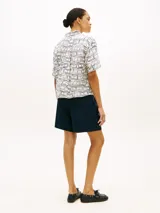 Camisa de manga corta Tommy Hilfiger de corte amplio y hombros ligeramente caídos, confeccionada en puro lino blanco con estampado geométrico de líneas azules. Cuenta con cuello inglés, cierre frontal de botones, bolsillo de parche en el pecho y logo bordado.