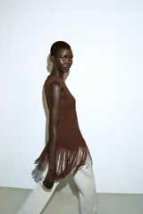 Top de cuello redondo y manga sisa, color marrón, con bajo asimétrico de flecos combinados a tono.