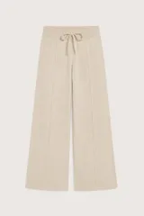 Pantalón de punto color beige, de corte recto y holgado, con cintura elástica y cordón ajustable. Presenta costuras verticales decorativas en el frente.