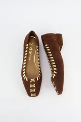 Mocasines de gamuza color marrón con detalles bordados en color dorado a lo largo del borde y en la puntera. Poseen un taco bajo de 2 cm.
