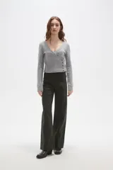 Sweater de punto gris con cuello en V, diseño cruzado y cierre lateral con botones. Presenta mangas largas y un ajuste al cuerpo con detalle acanalado en la cintura.