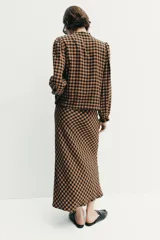 Falda midi de tiro alto con estampado de cuadros vichy en tonos marrón y negro. Presenta cintura elástica y un cinturón fino a contraste con hebilla metálica.