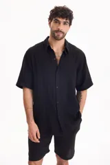 Camisa de muselina negra de manga corta, con cuello camisero y cierre frontal de botones.