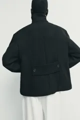Abrigo corto de paño con mezcla de lana, color negro. Presenta cuello subido con cierre de botones, manga larga y dos bolsillos de plastrón con solapa en el frente. Cierre frontal con botones.