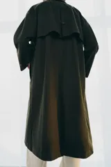 Trench oversize de color verde oscuro, con cuello de piel en tono marrón a contraste. Presenta manga larga con trabillas en los puños, bolsillos delanteros, cierre frontal con cremallera y botones ocultos bajo solapa, y abertura en la espalda.