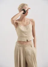 Pantalón Deia de corte recto y largo, color beige, con detalle de pinzas, trabillas y bolsillos laterales. Cuenta con cierre oculto de botón, gancho y cremallera, y forro interior.