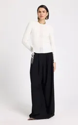 Sweater de punto fino color blanco, con cuello redondo y mangas largas. Presenta una textura acanalada con diseño de puntadas variadas y un detalle lateral de cordones trenzados con cierre de lazo y punteras metálicas.