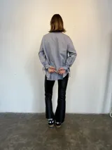 Camisa a rayas verticales azules y blancas, de popelina de algodón, con cuello verde y botones marmolados a tono. Es corta adelante y larga atrás.