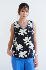 Top sin mangas de color blanco con escote en V y diseño holgado. Presenta un estampado artístico frontal en tonos azul y rojo, con terminaciones de vivo a contratono en color marrón.