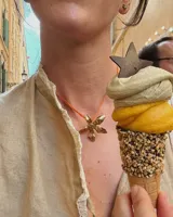 Collar artesanal con dije de flor en bronce o alpaca, suspendido en un cordón de seda natural teñido a mano. El diseño permite atarse con un moño, ofreciendo versatilidad para lucirlo de distintas formas.