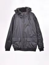 Campera negra con capucha con borde de piel sintética, cierre frontal con cremallera, bolsillos laterales con solapa y bolsillo con cremallera en la manga.