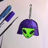 Par de aros colgantes con forma de cabeza de alienígena con pelo corto.