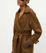 Trench coat largo de gamuza sintética con cuello peaked, cierre frontal cruzado con botones y cinturón ajustable en la cintura. Presenta mangas largas con reguladores en los puños y forro interior.
