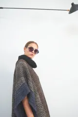 Poncho marrón con diseño de espiga en tonos beige y azul. Tiene cuello alto negro y flecos en el ruedo.