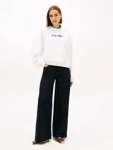 Buzo de felpa blanco de Tommy Hilfiger con cuello redondo, manga larga y calce regular. Cuenta con el logotipo de la marca bordado en tipografía script en el pecho y botones dorados decorativos en el hombro.
