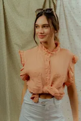 Blusa color salmón sin mangas, con volados en los hombros, cuello alto con ribete fruncido y cierre frontal con botones.