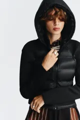 Chaqueta acolchada negra con cuello subido y capucha ajustable con cordones elásticos y stopper. Mangas largas combinadas en tejido efecto neopreno. Bolsillos laterales y cierre frontal con cremallera termosellada.