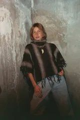 Poncho de lana con cuello alto y diseño de rayas verticales en tonos degradados de gris y negro. Presenta flecos en todo el borde inferior y laterales.
