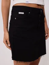 Falda de jean color negro, de corte recto y tiro medio, con ruedo deshilachado y cierre frontal con botón metálico.