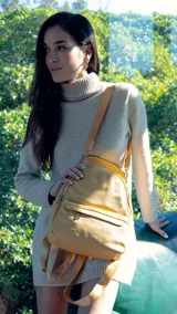 Mochila de tamaño mediano en color amarillo, confeccionada en símil cuero. Presenta un compartimento principal con cierre metálico, un bolsillo frontal con cierre y broche, y bolsillos laterales. Incluye correas regulables para la espalda, asa de mano y una correa adicional para llevar al hombro.