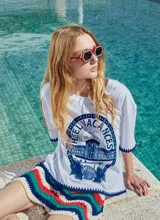 Remera blanca holgada con estampa exclusiva de un hotel y terminación en crochet azul en ruedo y mangas.