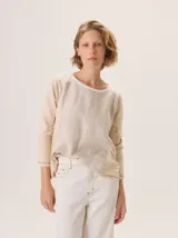 Remera de manga tres cuartos, con bloques de color y costuras expuestas en hilo contrastante. El cuerpo principal es beige claro, con un panel superior en blanco y un pliegue central en la espalda.