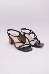 Sandalias negras de ecocuero con tiras finas que se cruzan en la capellada y se atan con nudos. Taco cuadrado simil madera.