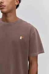 Remera de algodón color marrón con efecto lavado, de corte clásico y cuello redondo. Presenta un pequeño bordado de un pájaro en el pecho.