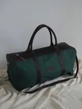 Bolso de lona color verde militar con detalles en cuero marrón. Tiene doble asa de mano y correa de hombro ajustable y extraíble.